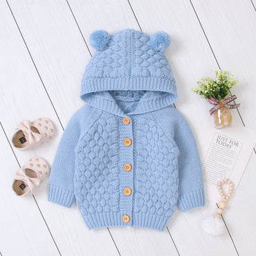 Blue knitted baby cardigan with hood on a white wooden floor.